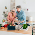 Senior,Couple,Preparing,Healthy,Smoothie,In,Kitchen,And,Using,Tablet