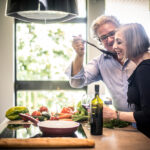 Senior,Couple,Cooking,Healthy,Food,And,Drinking,Red,Wine,At